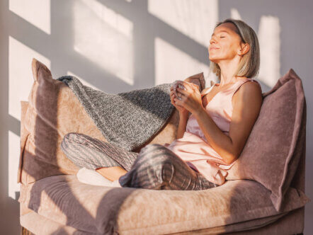 Adult woman sitting on the sofa at home and having a cup of coffee, relaxation concept