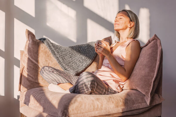 Adult woman sitting on the sofa at home and having a cup of coffee, relaxation concept