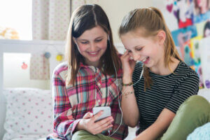 Two Girls Streaming Music From Mobile Phone In Bedroom