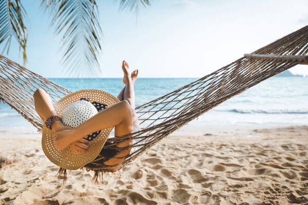 Holiday image, person in hammock on sandy beach. Source: AdobeStock_435196429