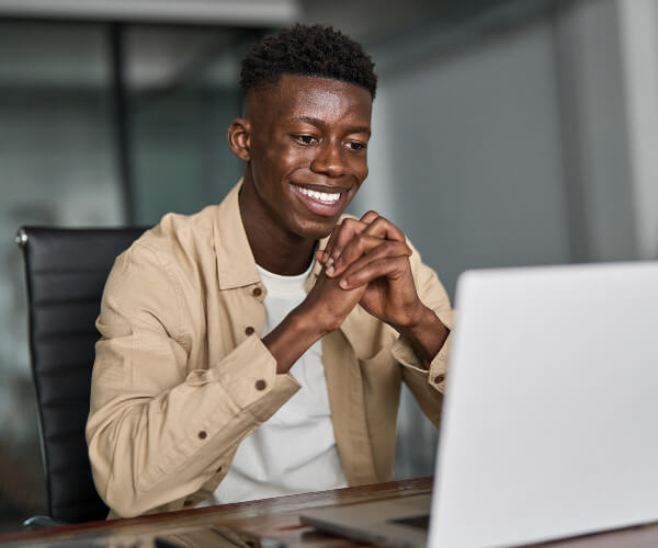 Happy young African ethnic business man looking at laptop working in office having virtual meeting. Smiling professional businessman employee or student using computer sitting at work desk - AdobeStock_1138851235 copy