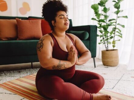 Attractive fitness woman with eyes closed practicing yoga in living room. Beautiful female in sports wear sitting crossed legs with eyes closed and hands joined at home.