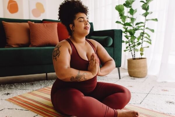 Attractive fitness woman with eyes closed practicing yoga in living room. Beautiful female in sports wear sitting crossed legs with eyes closed and hands joined at home.