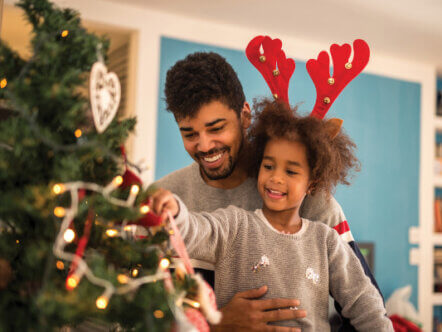 Dad and daughter decorating Christmas tree together.